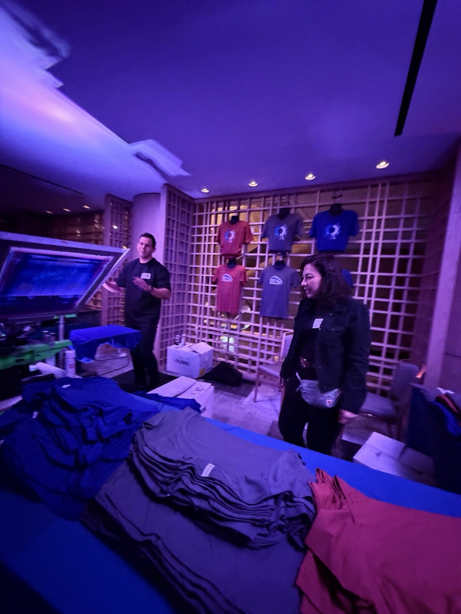Trade-show booth table with finished printed sample tees and caps on display at a Merch Troop live station
