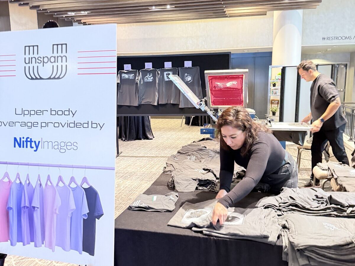 Crew member arranging folded freshly printed tees at a draped Merch Troop event merch table set up at a venue